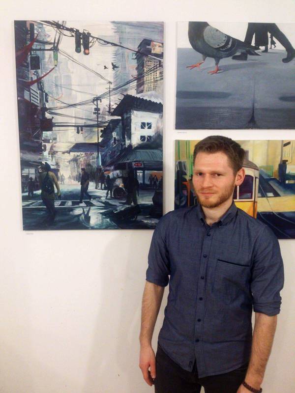 Andrzej Nogala stoi przodem do widza, a za nim wisi obraz. Obraz przedstawia futurystyczne miasto.